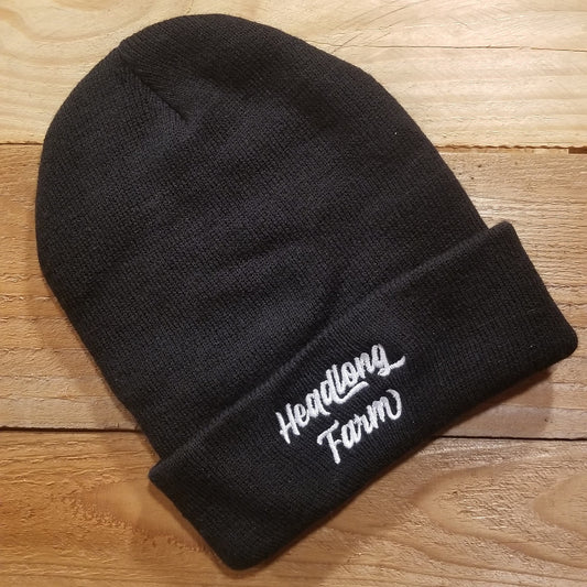 A black beanie embroidered with the Headlong Farm brand and a generous cuff