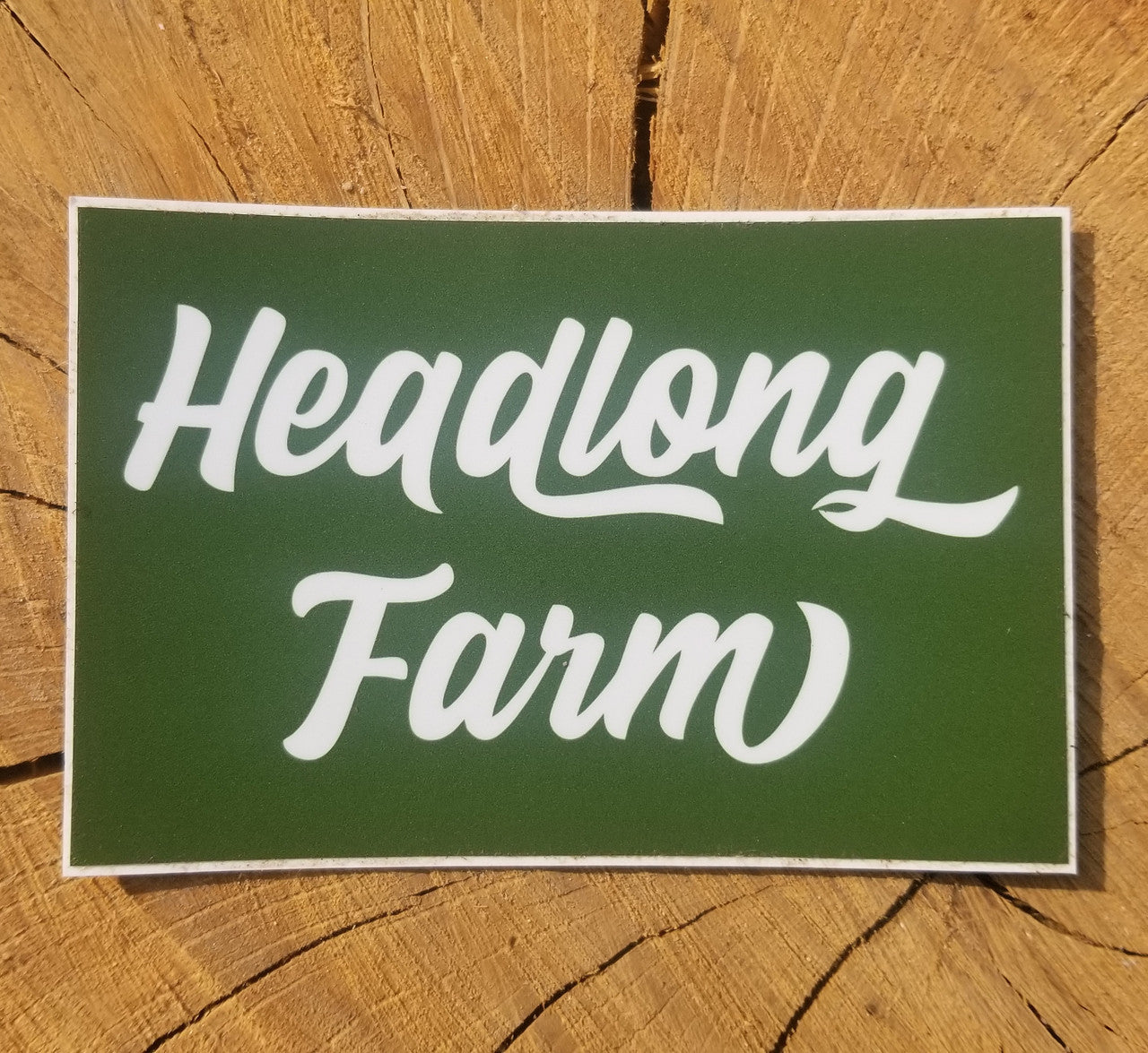 A square wordmark sticker with white text on green background, sitting on a piece of wood