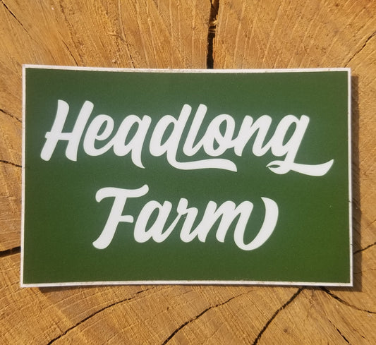 A square wordmark sticker with white text on green background, sitting on a piece of wood