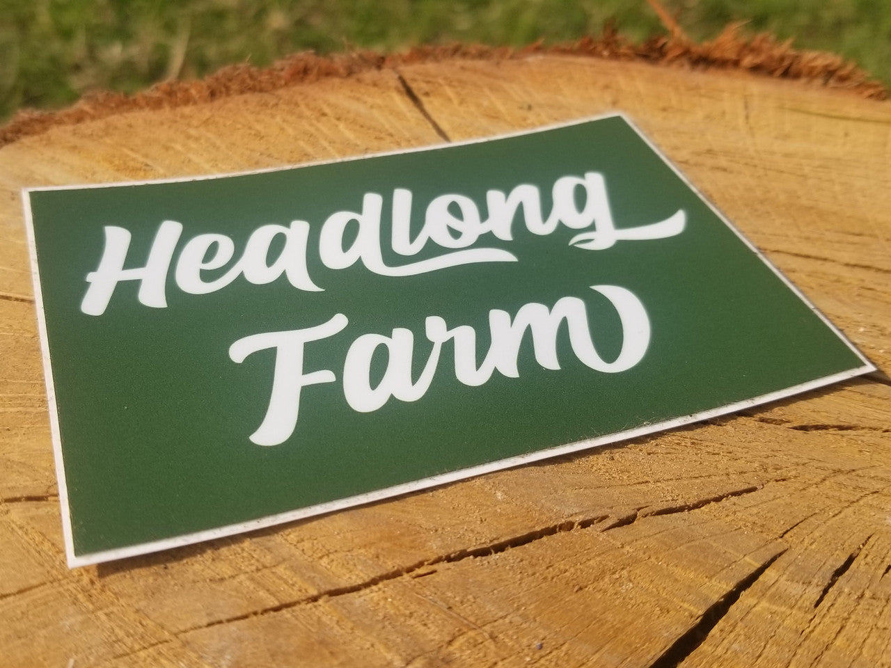 A square wordmark sticker with white text on green background, sitting on a piece of wood